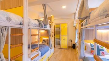 A dormitory room with bunk beds, wooden walls, and a yellow door.