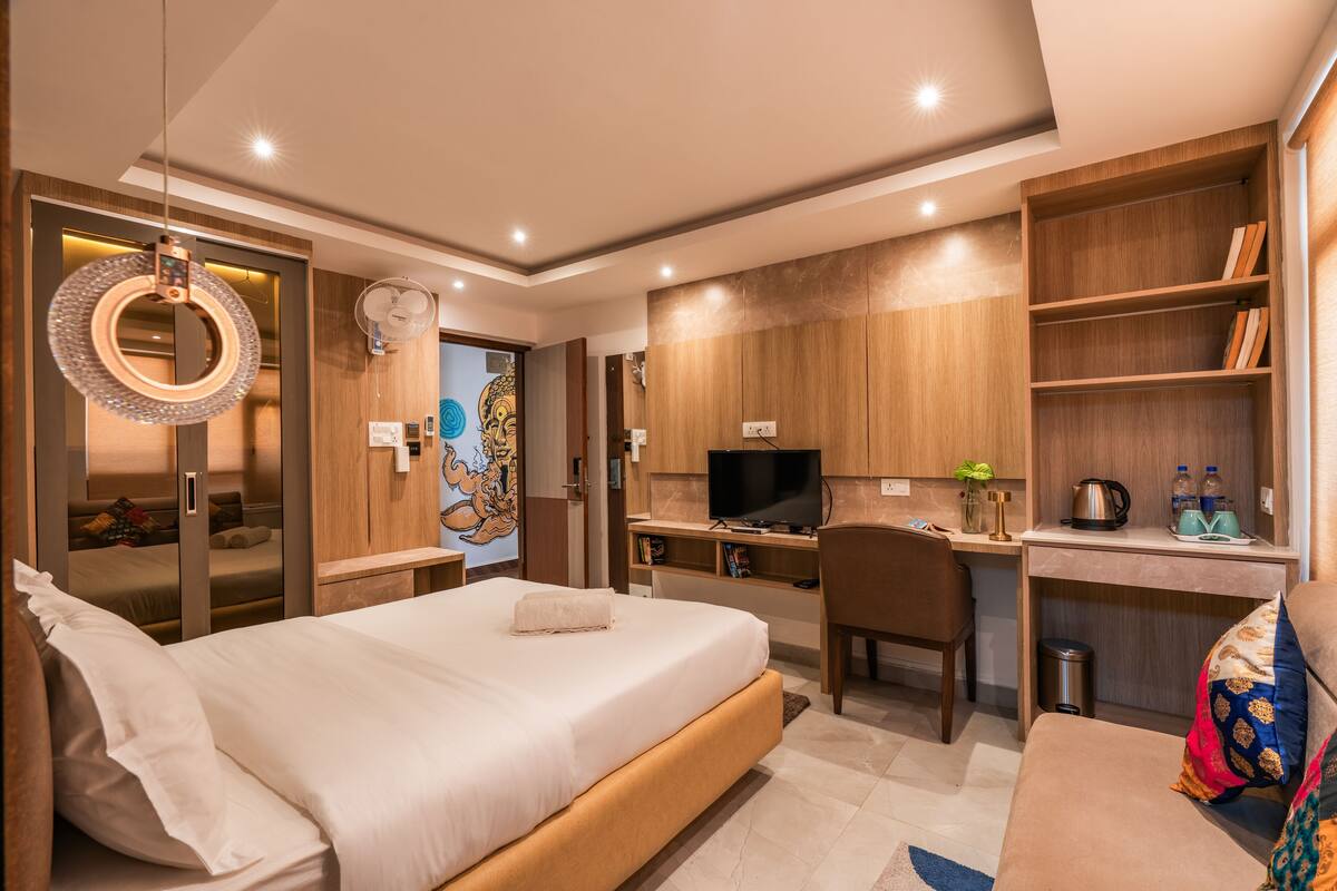 A modern hotel room with a bed, desk, TV, and built-in shelves.