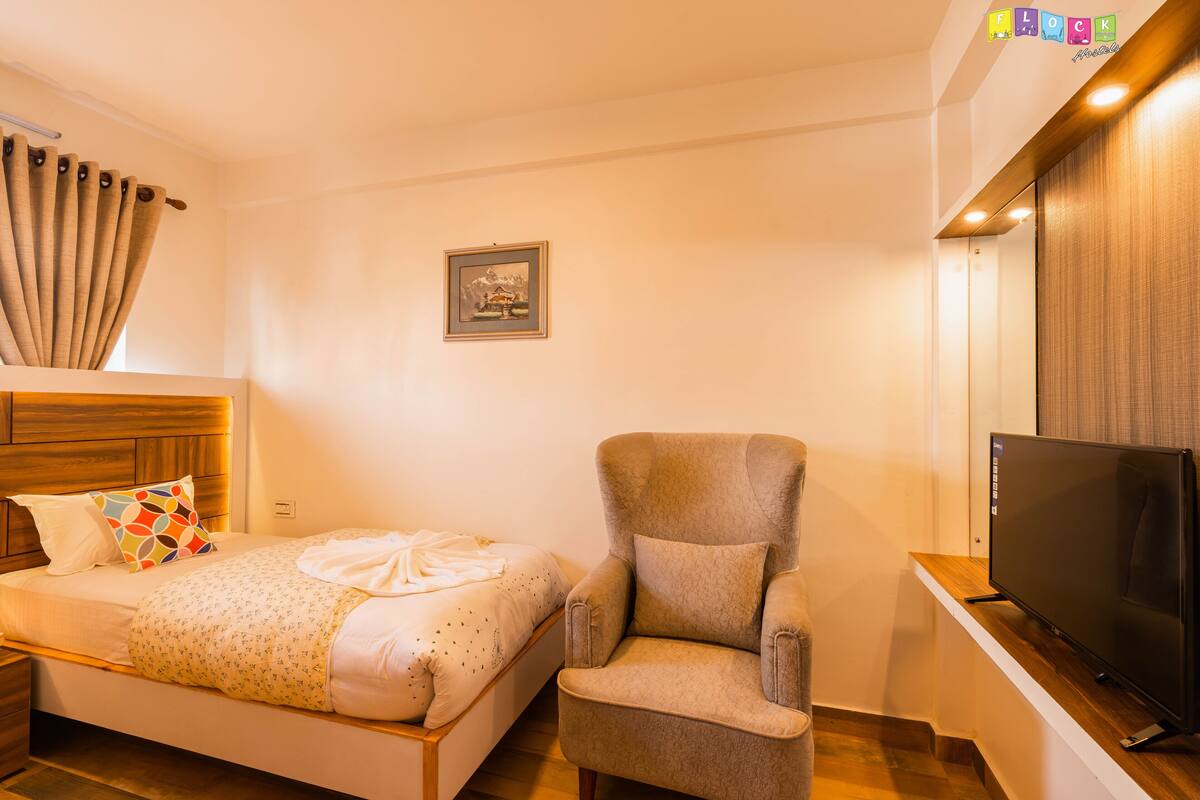 A hotel room with a bed, a chair, a TV, and a picture on the wall.