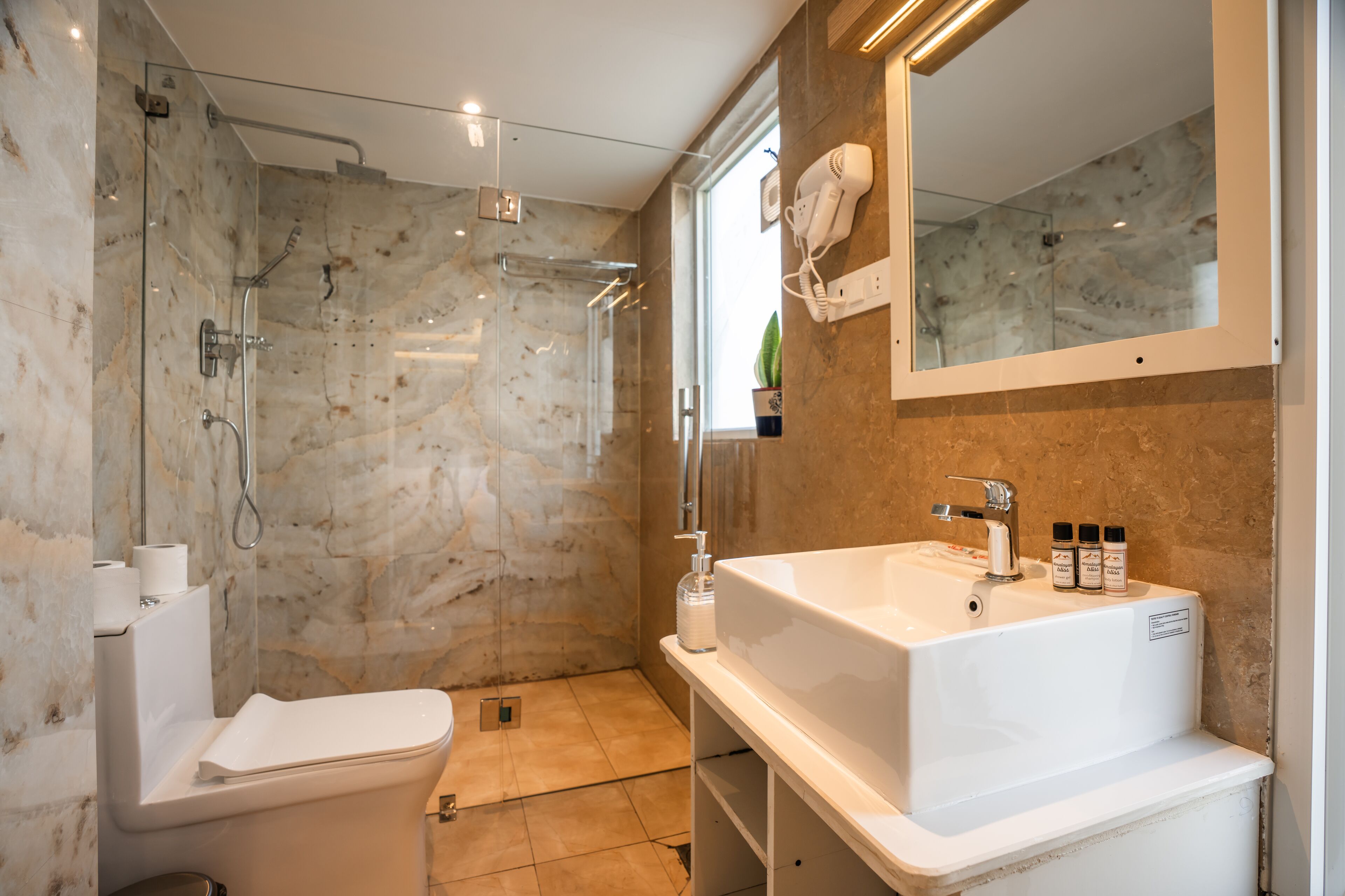 Een moderne badkamer met een douche met glazen wand, een wit wastafelmeubel met toiletartikelen en een grote spiegel.