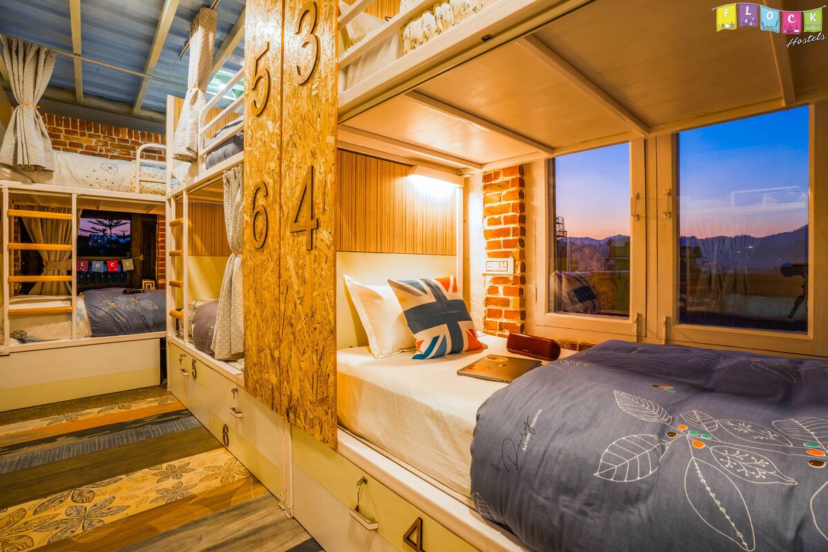 A bunk bed room with a brick wall, a window with a city view, and a wooden door.