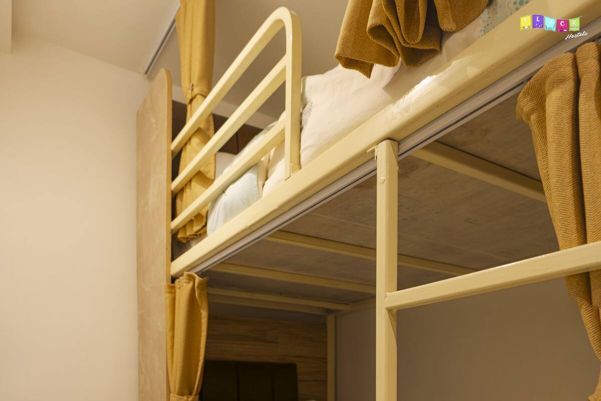 A bunk bed with a headboard, a pillow with an owl design, and a small table with a book. There is a backpack and a bicycle in the corner.