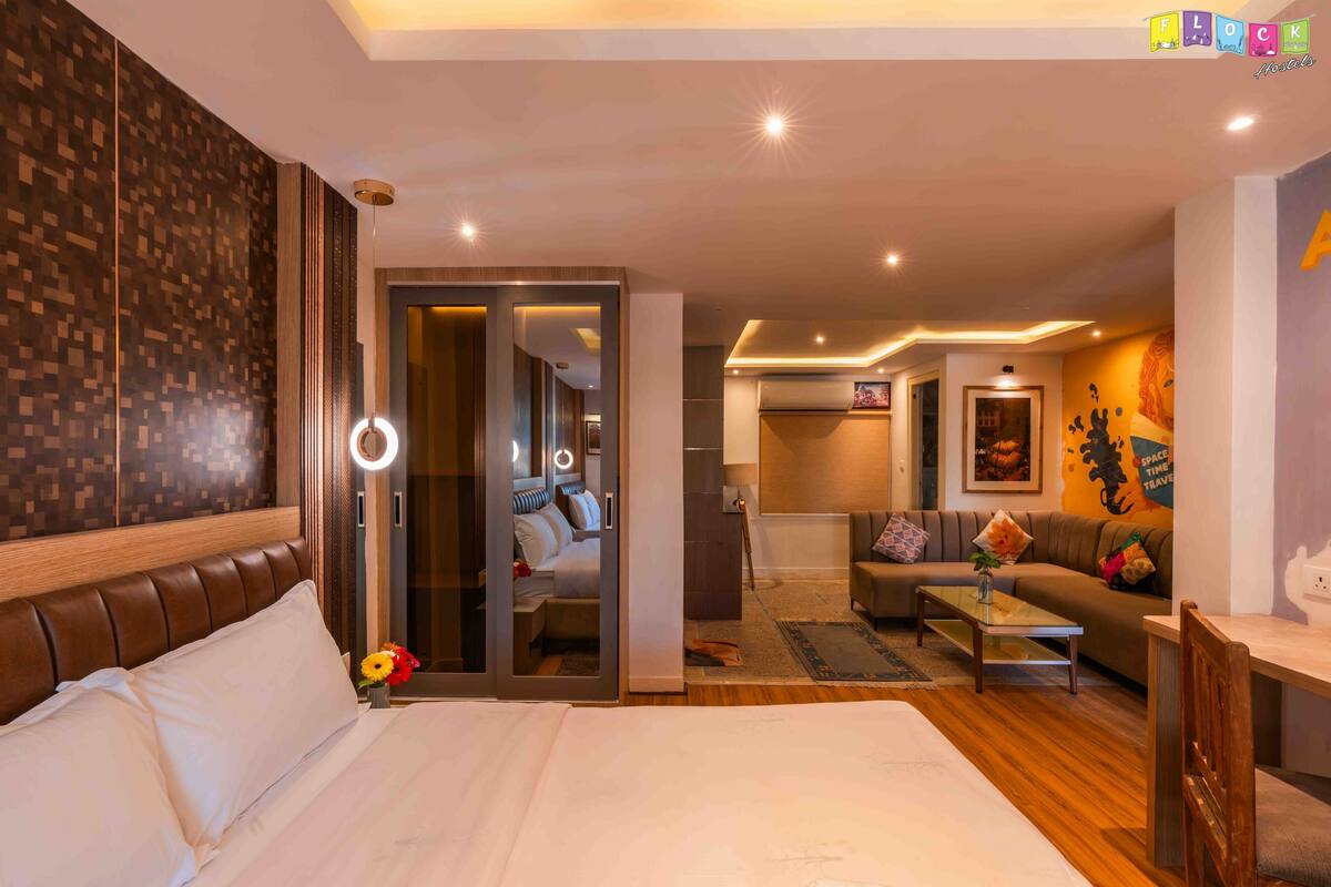 A hotel room with a large bed, a sitting area with a sofa and a coffee table, and a door leading to a hallway.