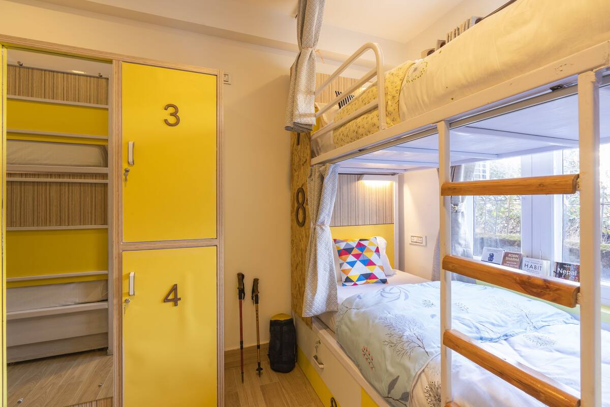A bunk bed with a window, a yellow wardrobe with multiple compartments, and a pair of trekking poles.