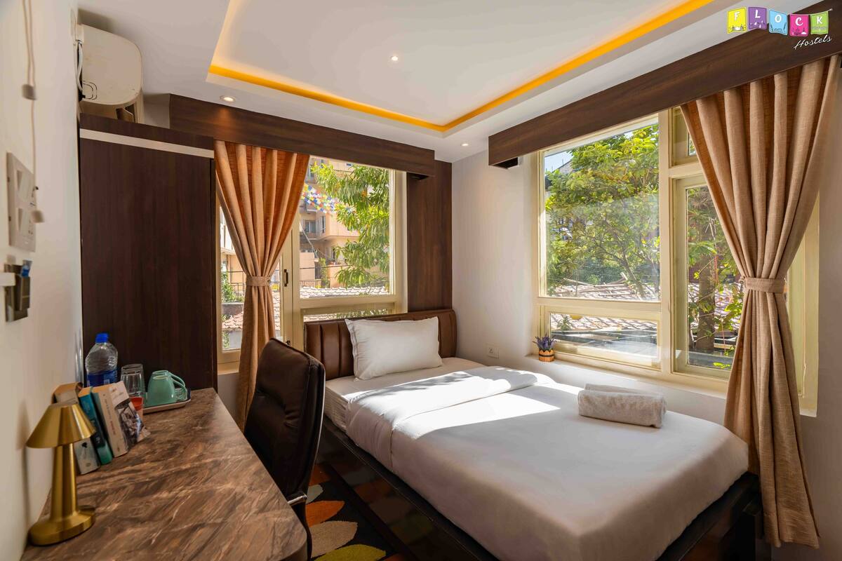 A hotel room with a bed, a desk, a chair, a window with curtains, and a view of the outside.