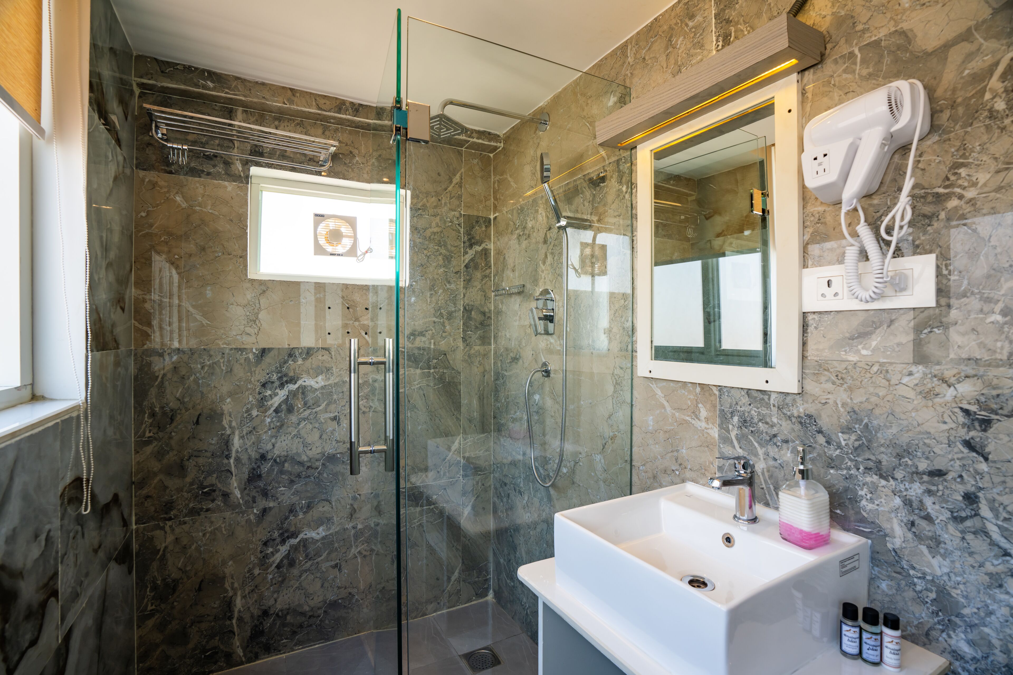 A modern bathroom with a glass-enclosed shower, a white sink, and a hairdryer mounted on the wall.