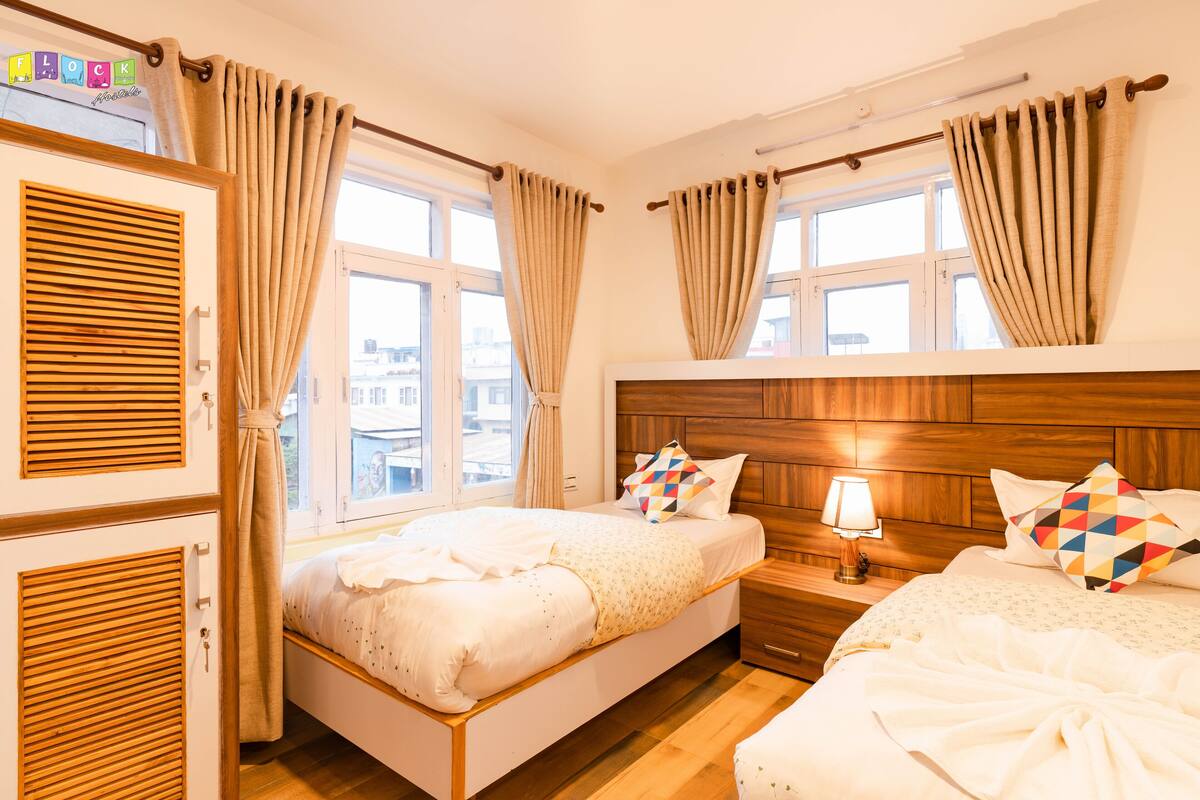 A hotel room with two beds, wooden headboards, a window with curtains, a bedside lamp, and a wardrobe.