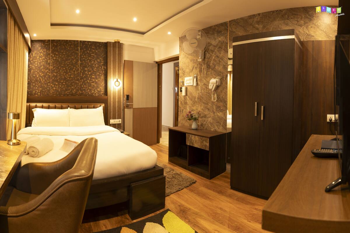 A hotel room with a bed, desk, chair, wardrobe, and a mirror.
