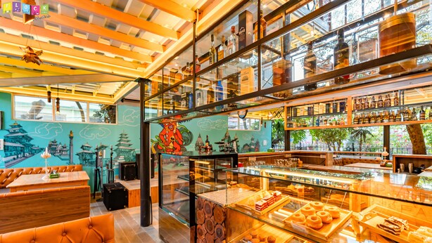 A bakery with wooden shelves, a display case with pastries, and a mural of a pagoda. - Flock Kathmandu (Kathmandu)