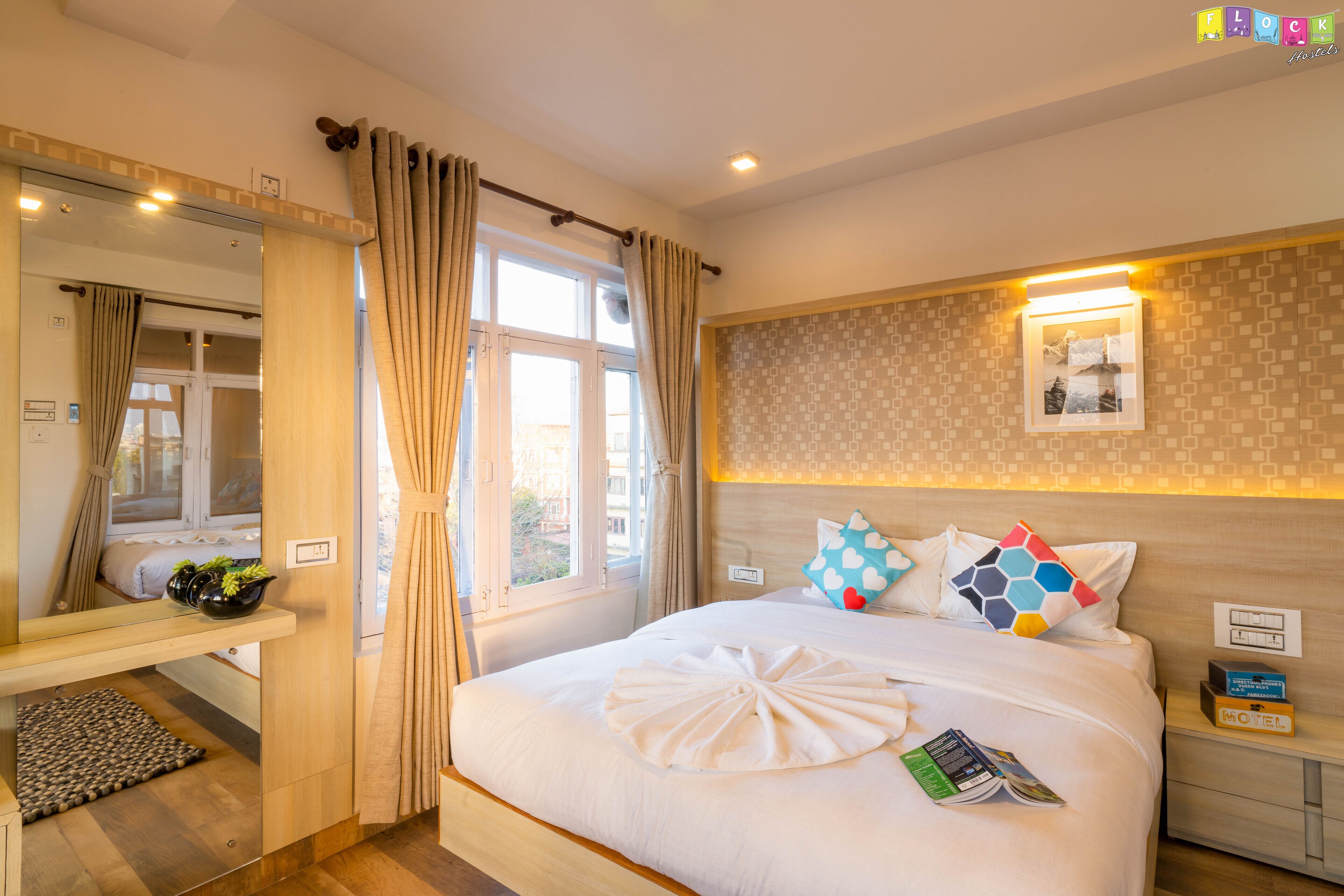 A hotel room with a large bed, a bedside table, a mirror, and a window with curtains.