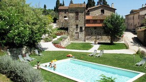 A swimming pool surrounded by grass and trees, with stone buildings in the background. - Cosy apartment in villa for 3 people with pool, WIFI, TV, patio and pets allowed (Sesto Fiorentino)