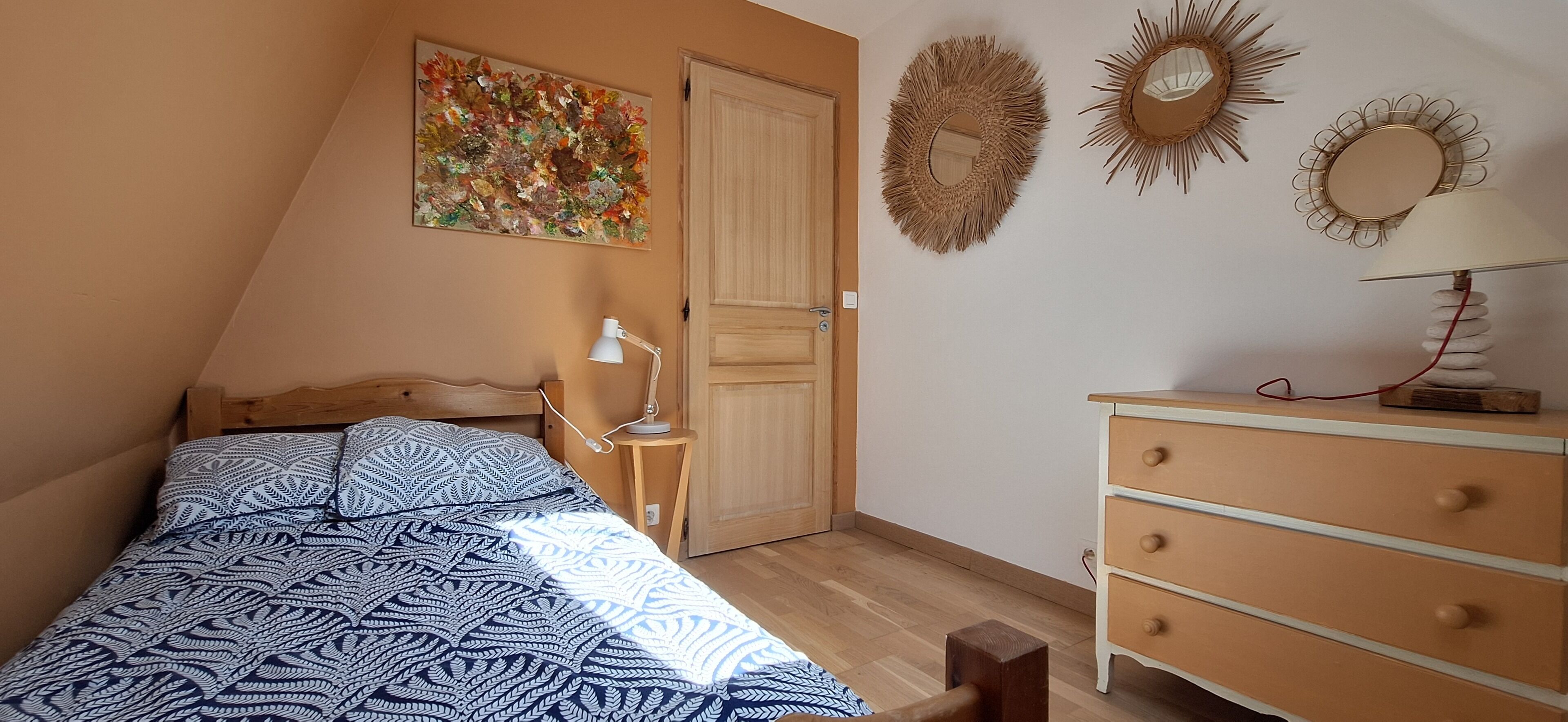 A bedroom with a bed, a dresser, a lamp, and decorative wall art.