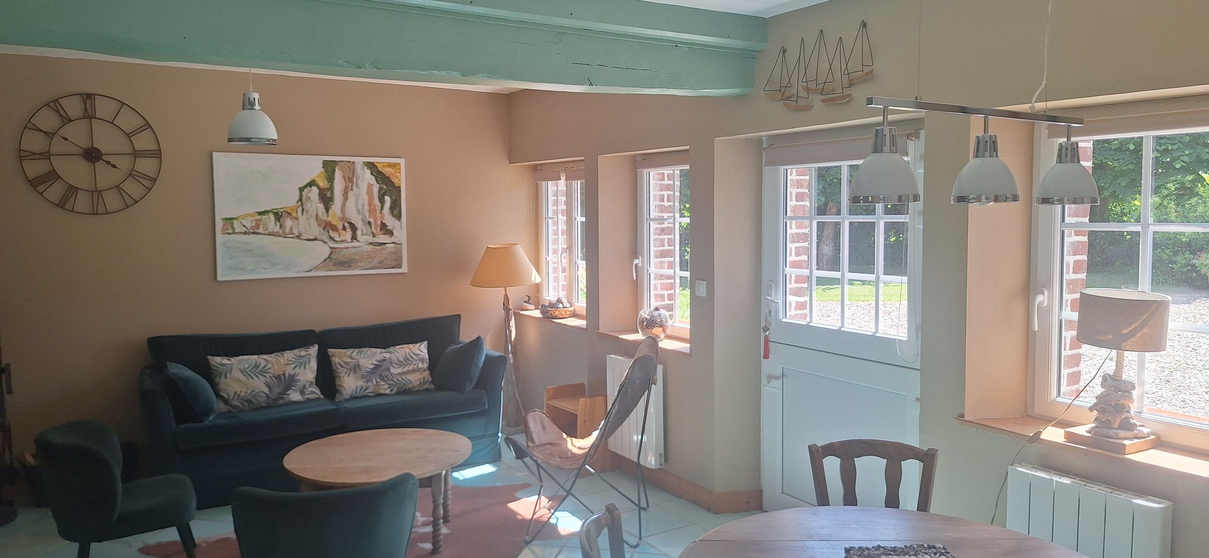 Una sala de estar acogedora con un sofá, una mesita redonda y un sillón. Hay un cuadro en la pared y una ventana con vistas al verdor exterior.