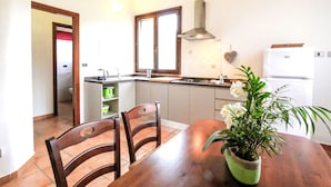 Una cucina compatta con piano cottura, lavello e frigorifero. C'è un tavolo con sedie e una pianta in vaso.