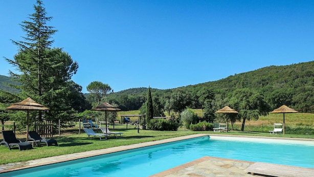 Una piscina con lettini e ombrelloni, circondata dal verde e da colline.