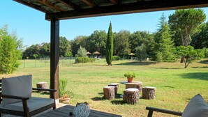 Un'area patio esterna con mobili in legno, tra cui sedie e un tavolo, e vista su un prato alberato.