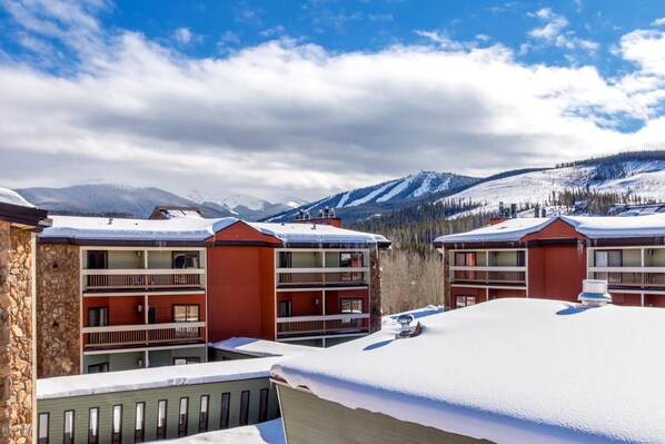 A row of red multi-story buildings with balconies, set against a snowy mountain backdrop.