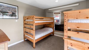 A bunk bed room with a framed picture on the wall, a small wooden dresser, and a window with a view of a building. - Beautiful 2 bd/2 ba condo in the heart of town with all the amenities (Winter Park)