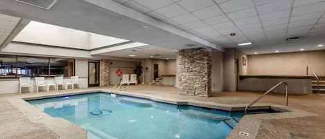 An indoor swimming pool with a stone pillar, a lifebuoy, and a bar area with chairs.