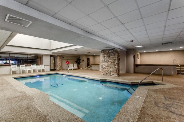 An indoor swimming pool with a stone pillar, a lifebuoy, and a bar area with chairs.