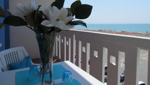 Una mesa con un jarrón de flores, un mantel azul y vistas a la playa y al océano.