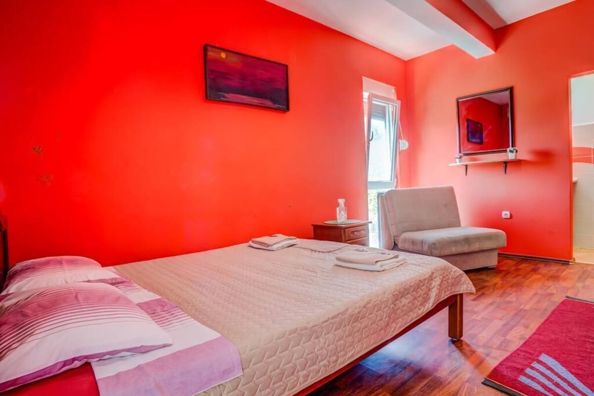 A bedroom with a bed, a chair, a small table, and a painting on the wall.