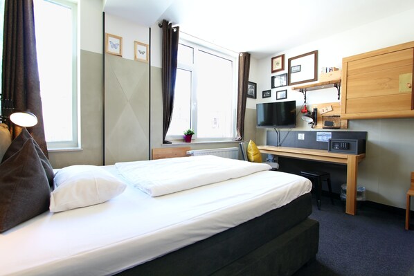 Una habitación de hotel con cama, escritorio, televisión y ventana con cortinas.