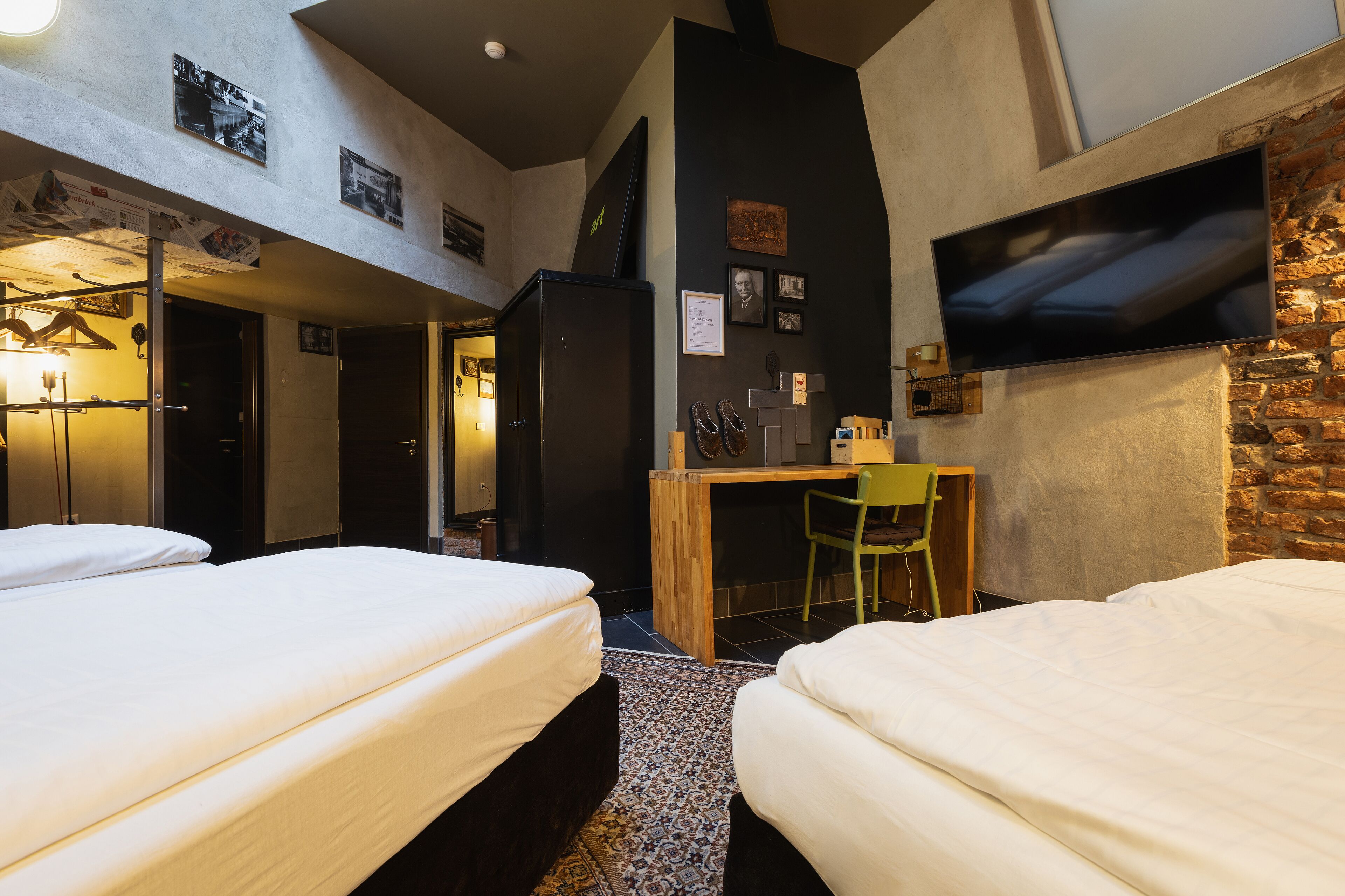 A hotel room with two beds, a desk, a TV, and a small kitchenette.