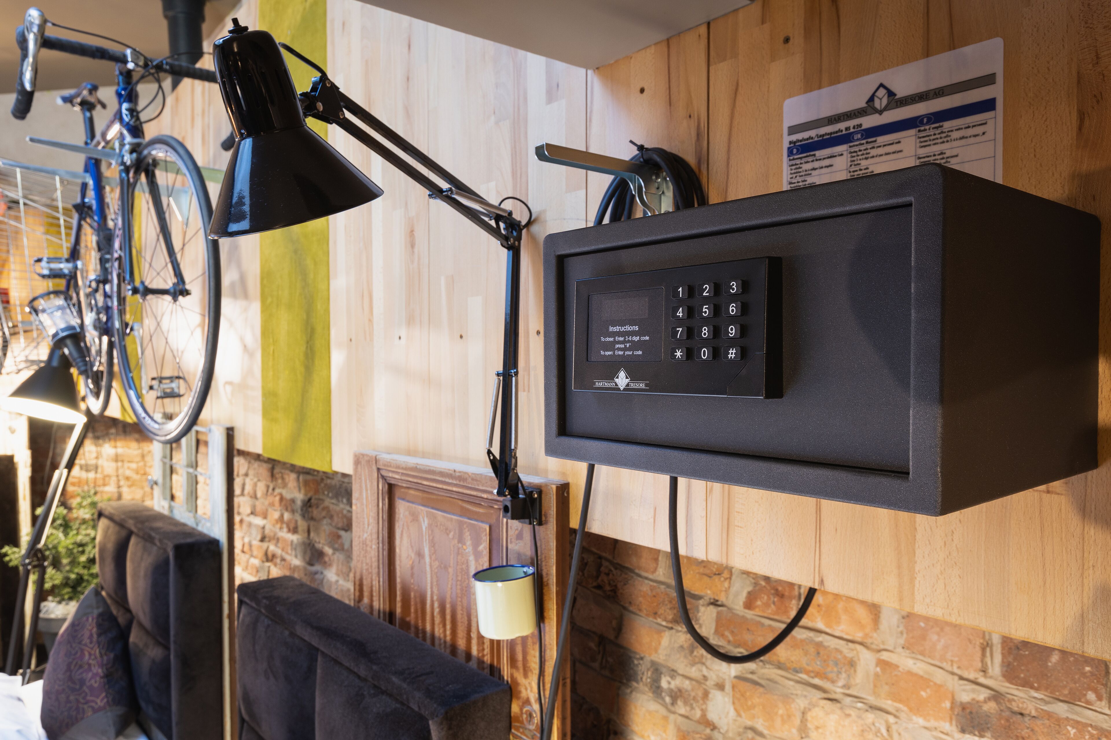 A room with a mounted bicycle, a desk lamp, and a thermostat control panel on the wall.