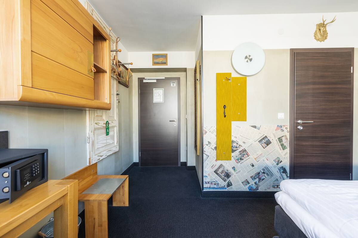 Hotelkamer met een bed, een houten bureau, een magnetron, een bankje, een deur met sleutelgat en een muur met een krantenkaart.