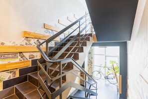 Een moderne trap met metalen leuningen en houten treden, die leidt naar een kamer met een fiets en een plant.