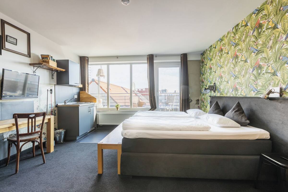 Een slaapkamer met een bed, een bureau, een stoel, een raam en een muur met een tropisch patroon.
