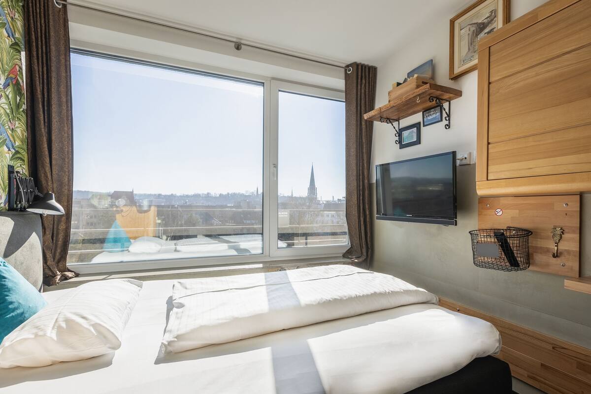 Een hotelkamer met een groot raam, een bed, een televisie en een houten kast.