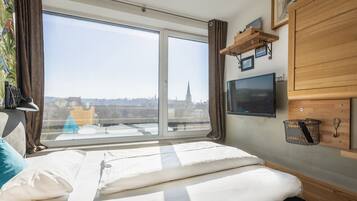 Een hotelkamer met een groot raam, een bed, een televisie en een houten kast.