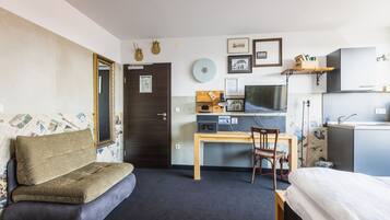 Une pièce de taille modeste comprenant un lit, un canapé, un bureau avec un ordinateur et une petite kitchenette.