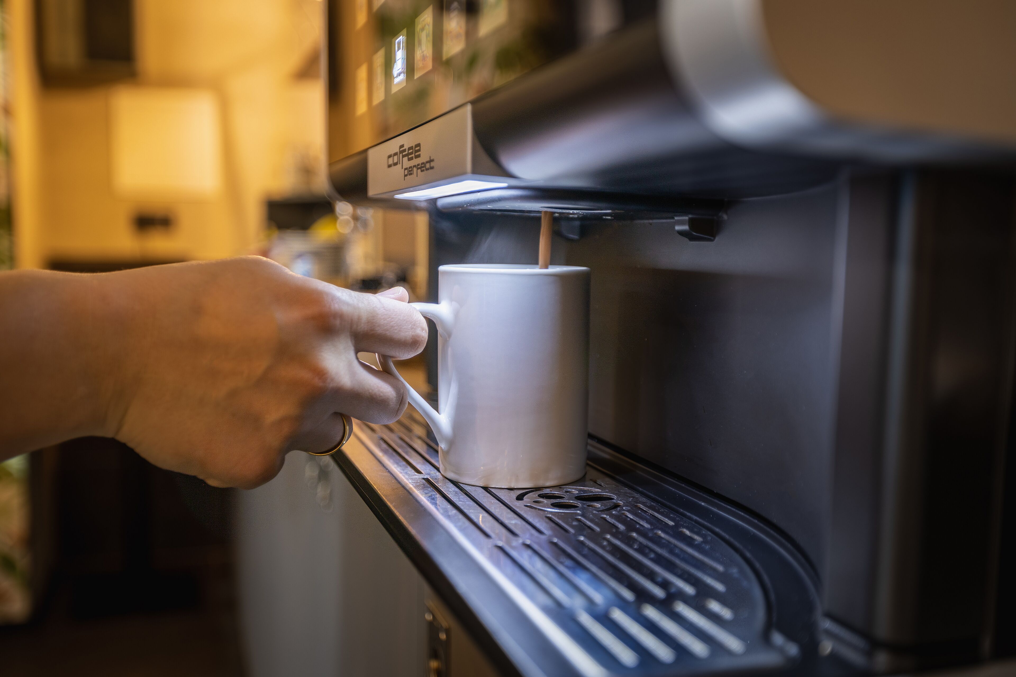 A hand placing a mug under a coffee machine.