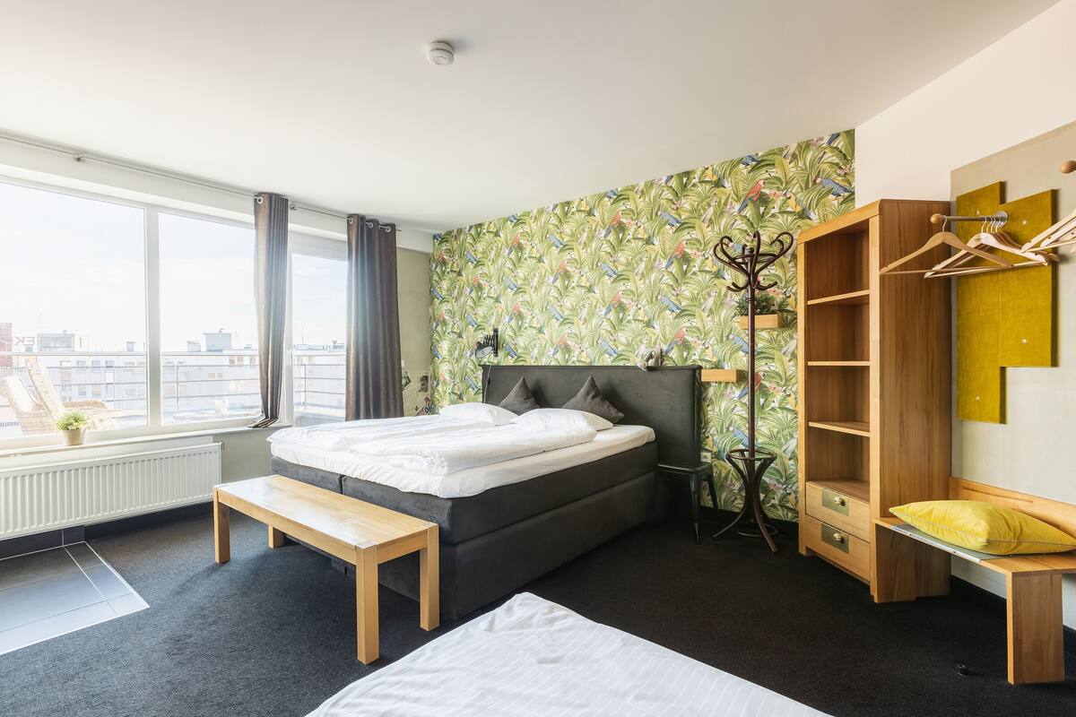 Een moderne slaapkamer met een groot bed, een bankje, een houten garderobe en uitzicht op de stad.