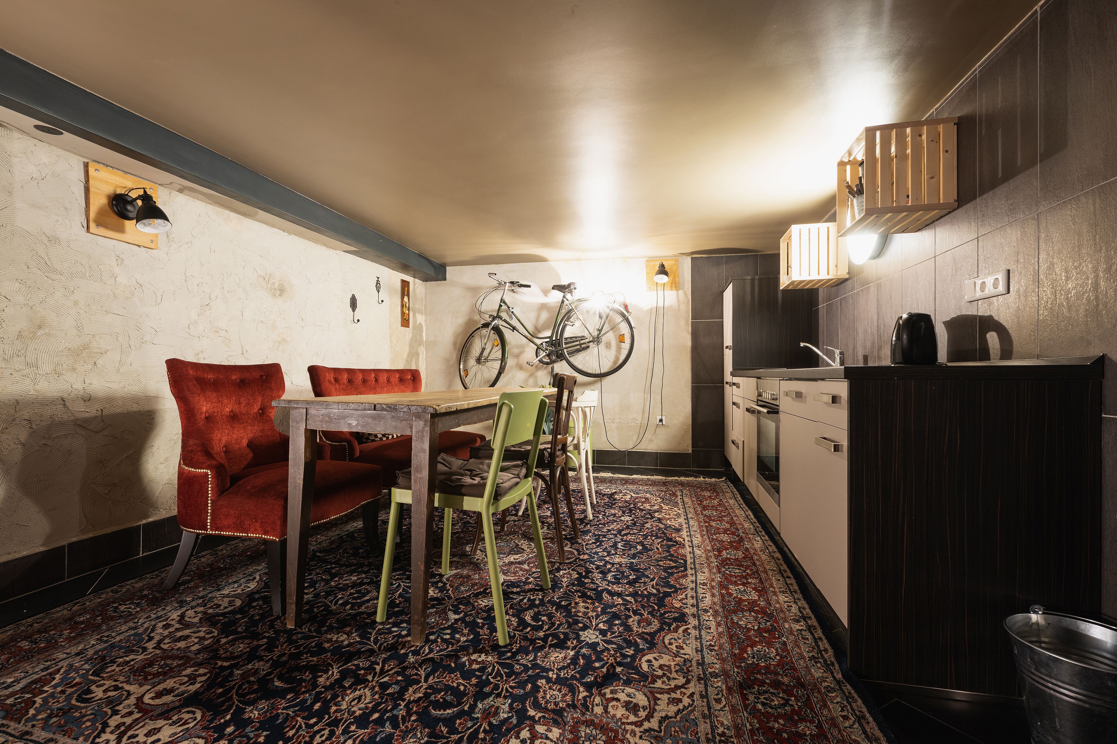 A compact kitchen with a dining area, a bicycle mounted on the wall, and a patterned rug.