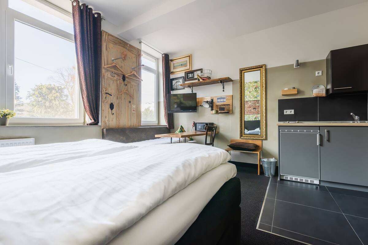 Een hotelkamer met een bed, een bureau, een stoel, een televisie, een spiegel, een kitchenette en een raam met gordijnen.