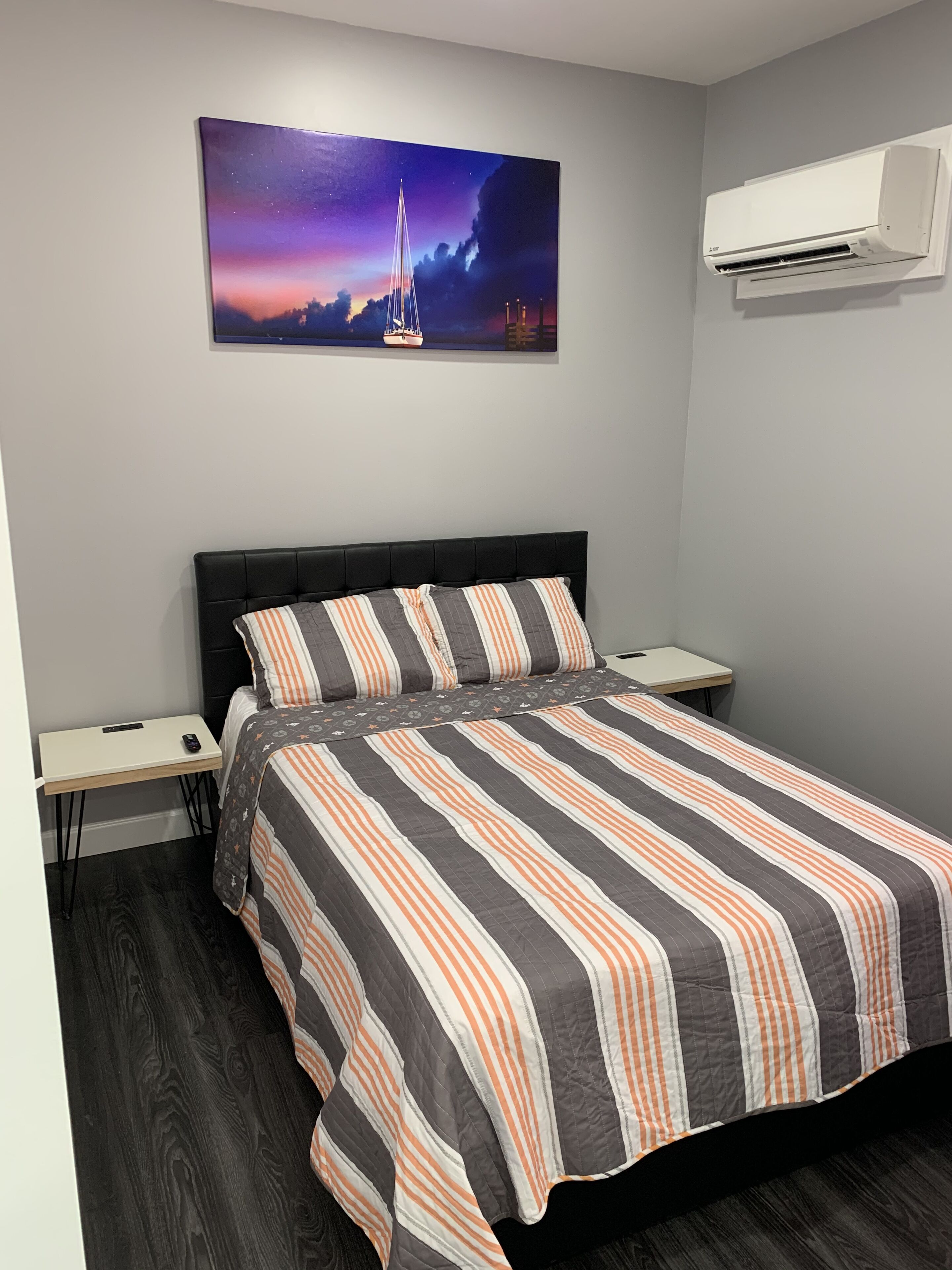 Un dormitorio con cama, mesita de noche, aire acondicionado de pared y un cuadro de un velero en la pared.