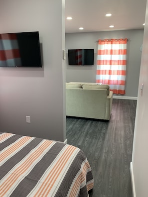 Una habitación con cama, televisión, sofá y ventana con cortinas.