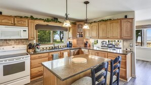 A modern kitchen with wooden cabinets, a granite countertop, and a large island with bar stools. - Tilghman | Pool | Private Dock | Pet Friendly (Tilghman)
