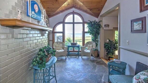 A cozy room with a stone floor, wicker furniture, and a large arched window offering a view. - Tilghman | Pool | Private Dock | Pet Friendly (Tilghman)