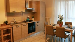 A modern kitchen with wooden cabinets, a stove, and a dining area with chairs and a table. - Bnbook- Via Torino Train Station (Rho)