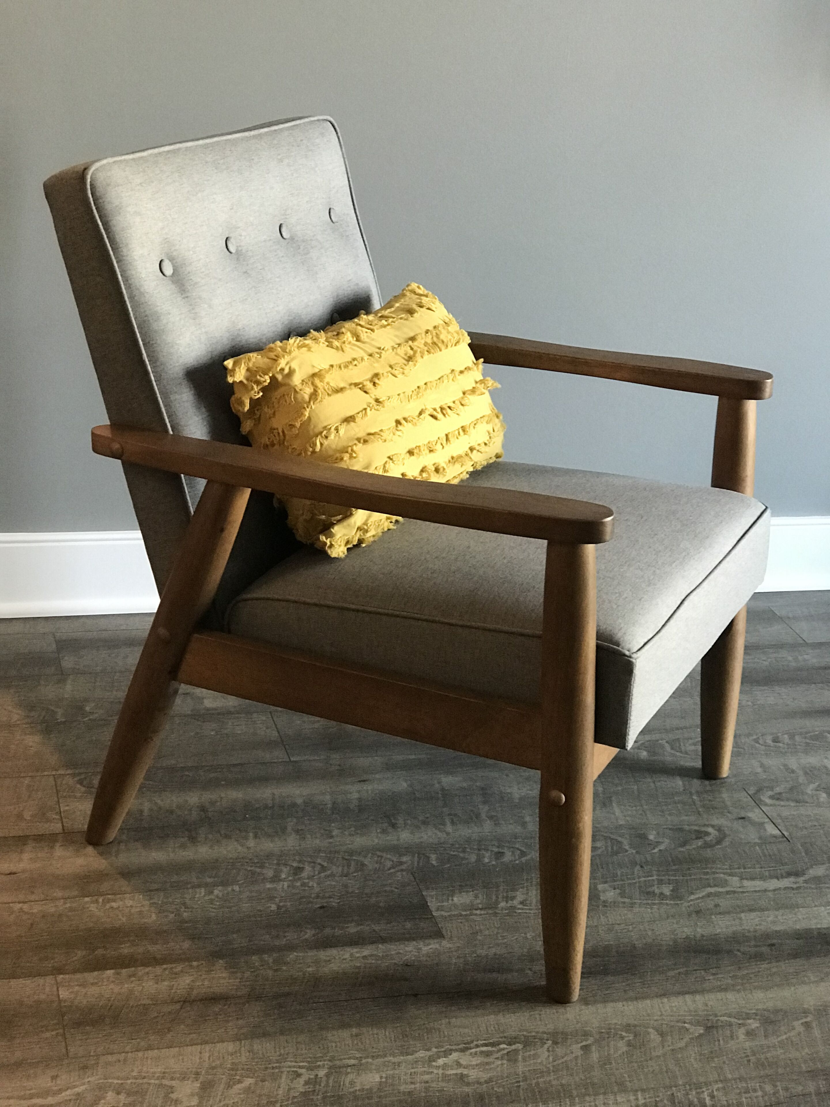 A wooden armchair with a grey upholstered seat and backrest, featuring a single yellow cushion.