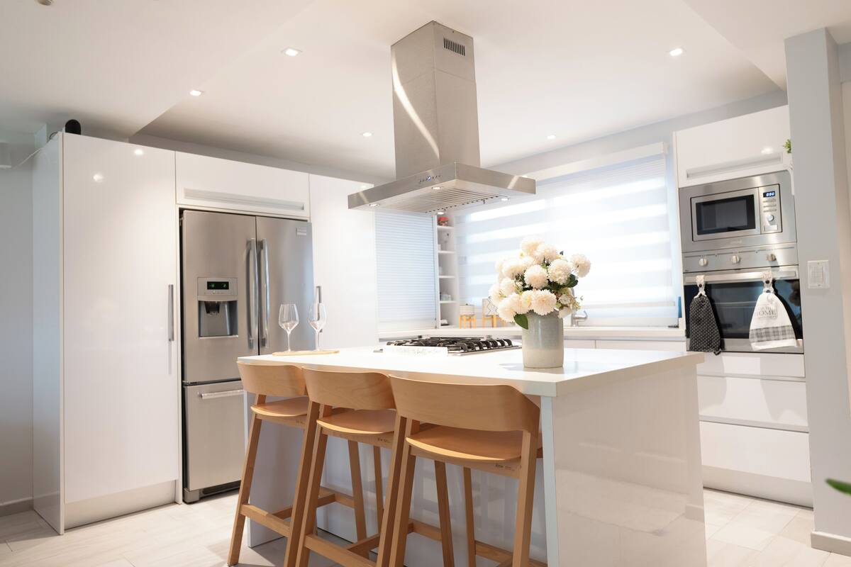 A modern kitchen with a central island, bar stools, stainless steel appliances, and a decorative vase with flowers.