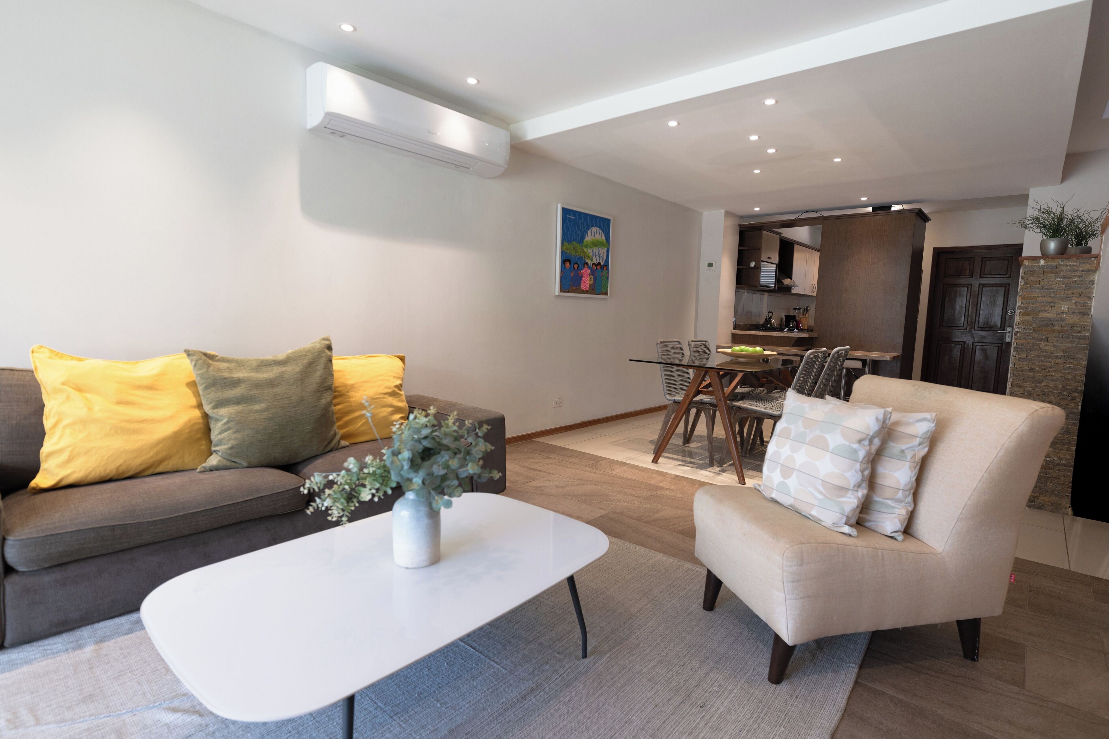 A modern living room with a sofa, armchair, and coffee table. There is a dining area with a table and chairs.