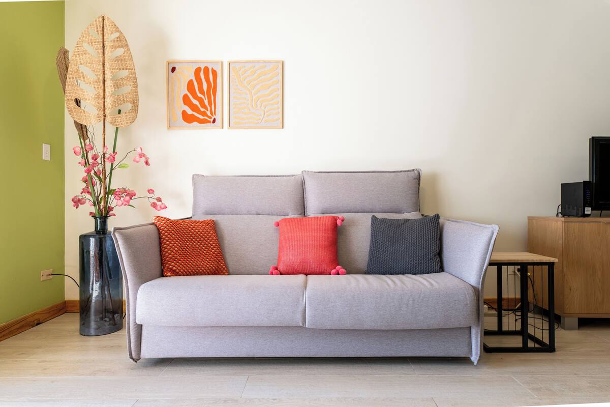 A living room with a grey sofa, a vase with pink flowers, and two abstract paintings on the wall.