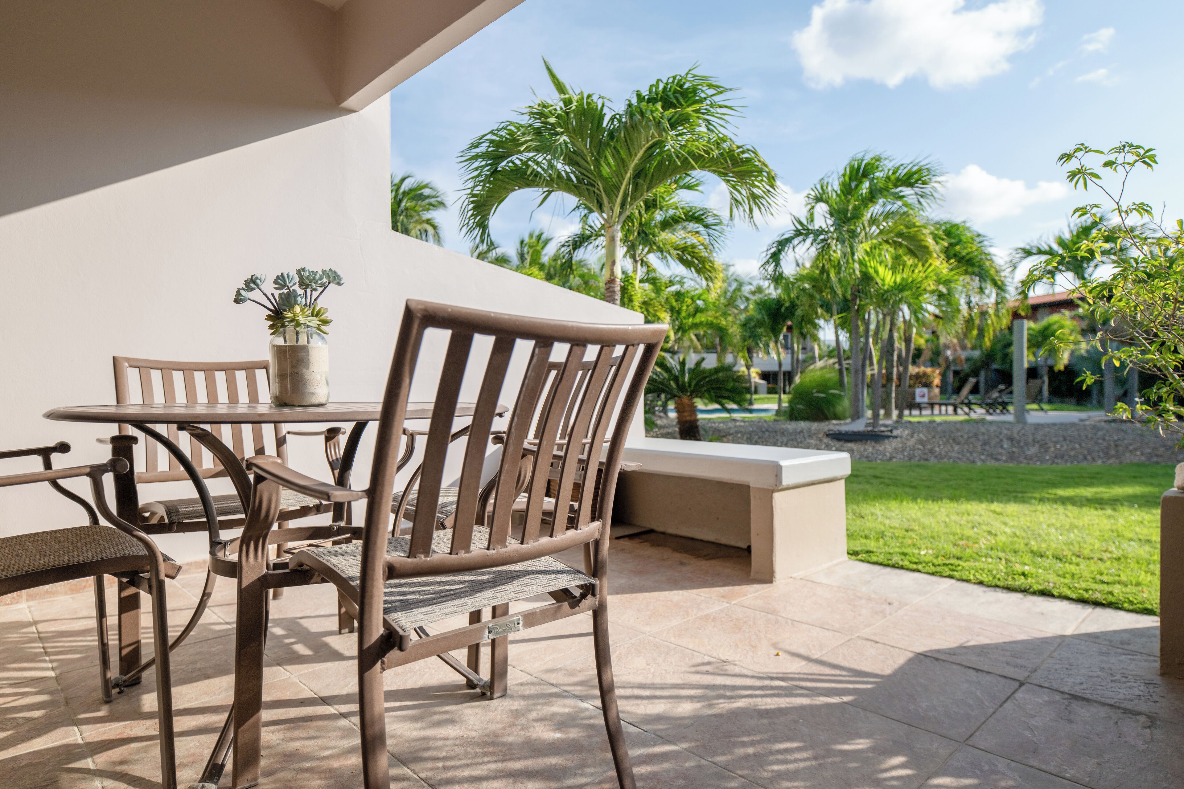 Un patio al aire libre con una mesa y sillas, una planta en maceta y vistas a palmeras y una zona de césped.
