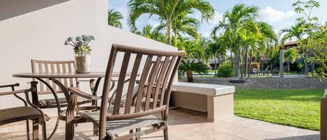 Un patio al aire libre con una mesa y sillas, una planta en maceta y vistas a palmeras y una zona de césped.